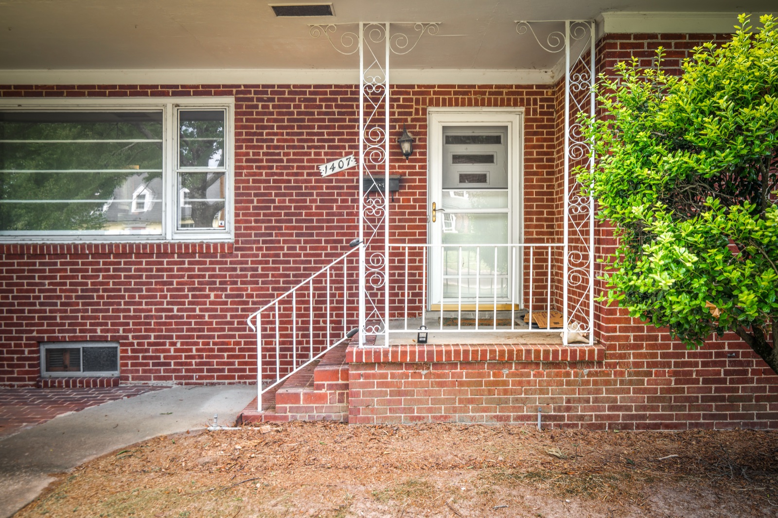 The covered front entry of 1407 Wentbridge Road, with original white wrought iron railings and brick steps