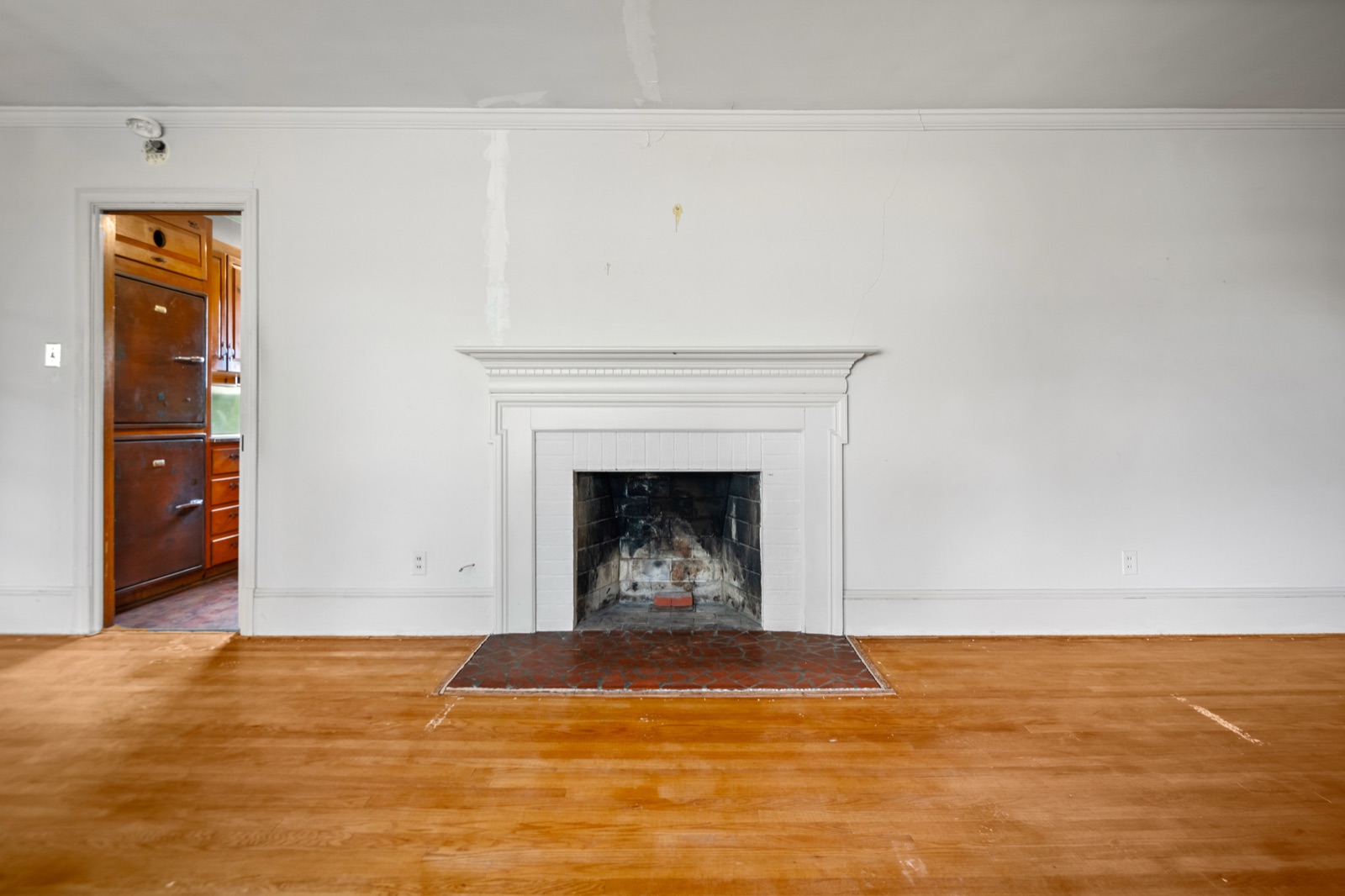 The living room fireplace, with the original built-in kitchen refrigerator visible through the doorway