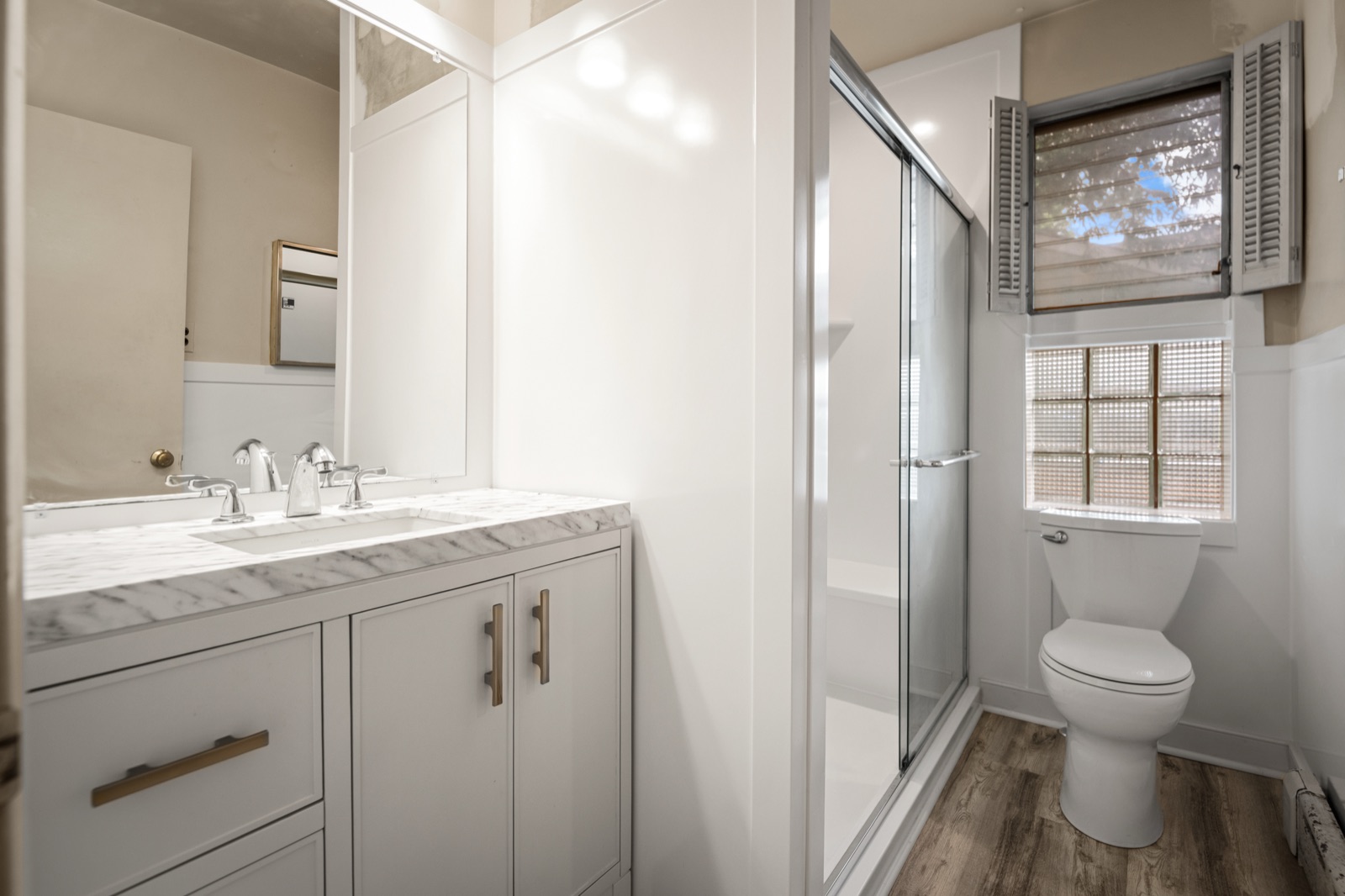 The updated main-level full bath, with a marble-top vanity and glass shower
