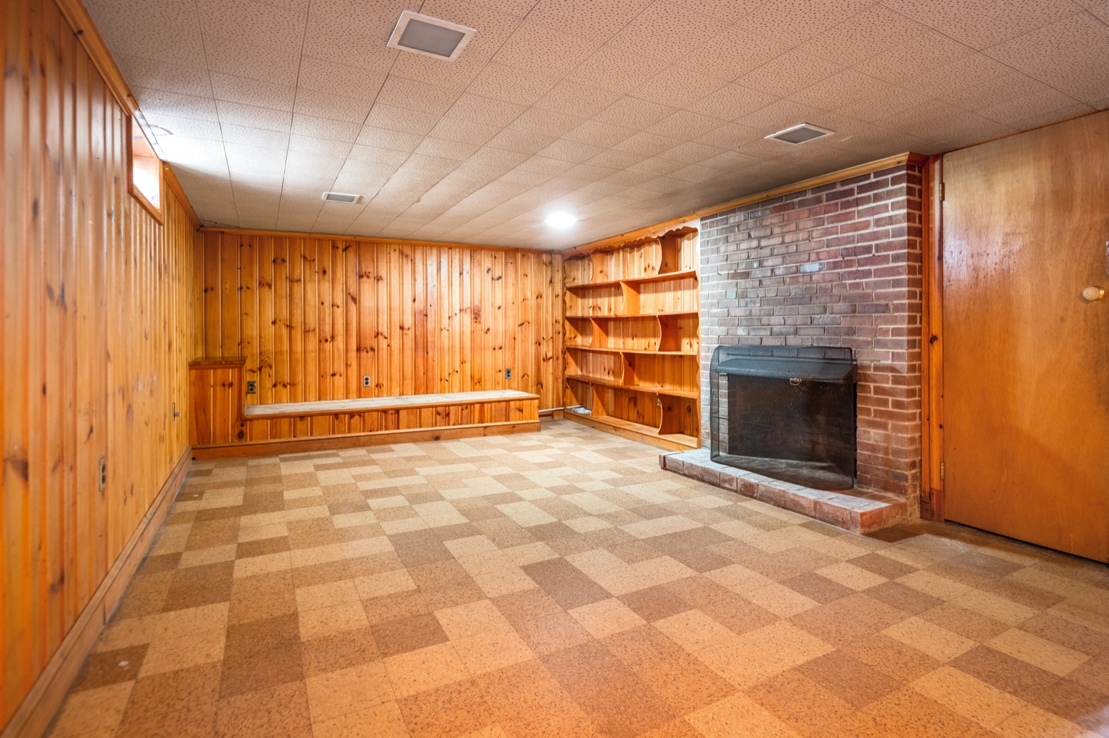 The lower-level recreation room, paneled in knotty pine with a second brick fireplace